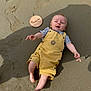 baby, child, sand, yellow_overalls, striped_shirt, barefoot, smiling, shadow, wooden_plaque, age_marker, outdoor, sunny, happy, cute, infant, reaching, skin, footprint, playful, summer