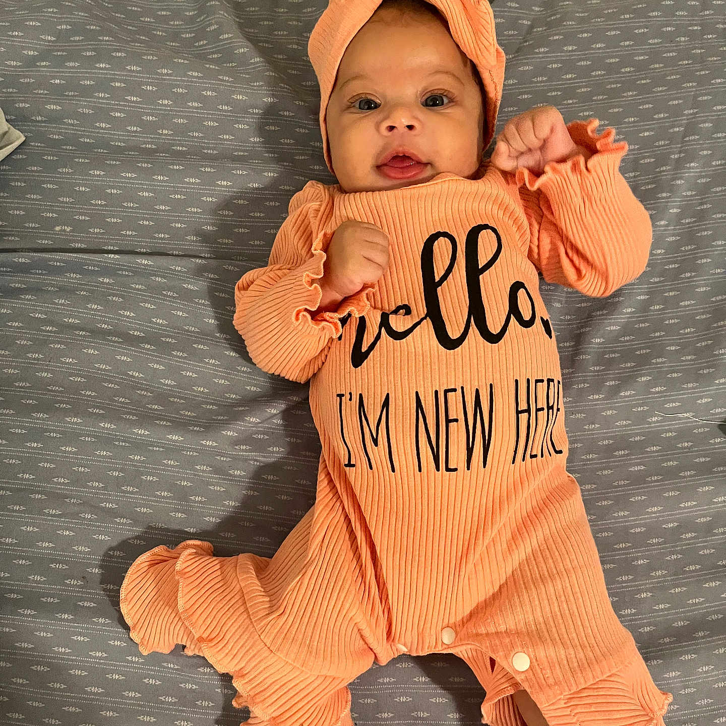 Dalani is registered to the contest to win money with this photo: adorable, baby, bed_sheet, child, clothing, cute, fabric_texture, headband, indoor, infant, lying_down, newborn, open_mouth, orange_outfit, patterned_sheet, person, portrait, sleepwear, smiling, wide_eyes