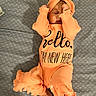 apparel, baby, blanket, child, comfortable, cozy, cute, foot, hands_near_face, headband, indoors, infant, lying_down, newborn, orange_outfit, patterned_blanket, portrait, resting, sleeping, soft_lighting