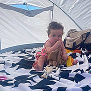 Luna participe au concours pour gagner de l'argent avec cette photo : baby, child, tent, blanket, toy, curly_hair, indoor, polka_dot_bag, colorful_toys, soft_toy, patterned_blanket, sitting, cute, natural_light, blue_sky, playtime, infant, pink_dress, foot, hand