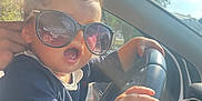 Luna participe au concours pour gagner de l'argent avec cette photo : child, toddler, sunglasses, car, steering_wheel, curly_hair, hand, sunlight, window, seat, clothing, person, portrait, expression, vehicle_interior, daylight, outdoor, reflection, casual, cute