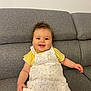 Luna participe au concours pour gagner de l'argent avec cette photo : baby, child, smiling, happy, sitting, curly_hair, yellow_shirt, white_dress, floral_print, couch, indoor, portrait, cute, infant, person, face, skin, hand, leg, comfortable