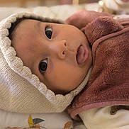 Zoé a rejoint le concours — aidez-le/la à gagner de superbes lots ! baby, close_up, face, hat, knit, brown_fleece, tongue_out, curious_eyes, infant, blanket, soft_texture, cute, indoors, warm_clothing, newborn, person, child, portrait, lying_down, cozy