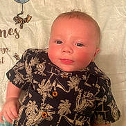 Kaleb Jr. is registered to the contest to win money with this photo: baby, infant, child, dinosaur_shirt, button_up, lying_down, blanket, patterned_blanket, cute, rosy_cheeks, smiling, tongue_out, short_hair, indoors, portrait, close_up, young_child, person, clothing, sleepwear