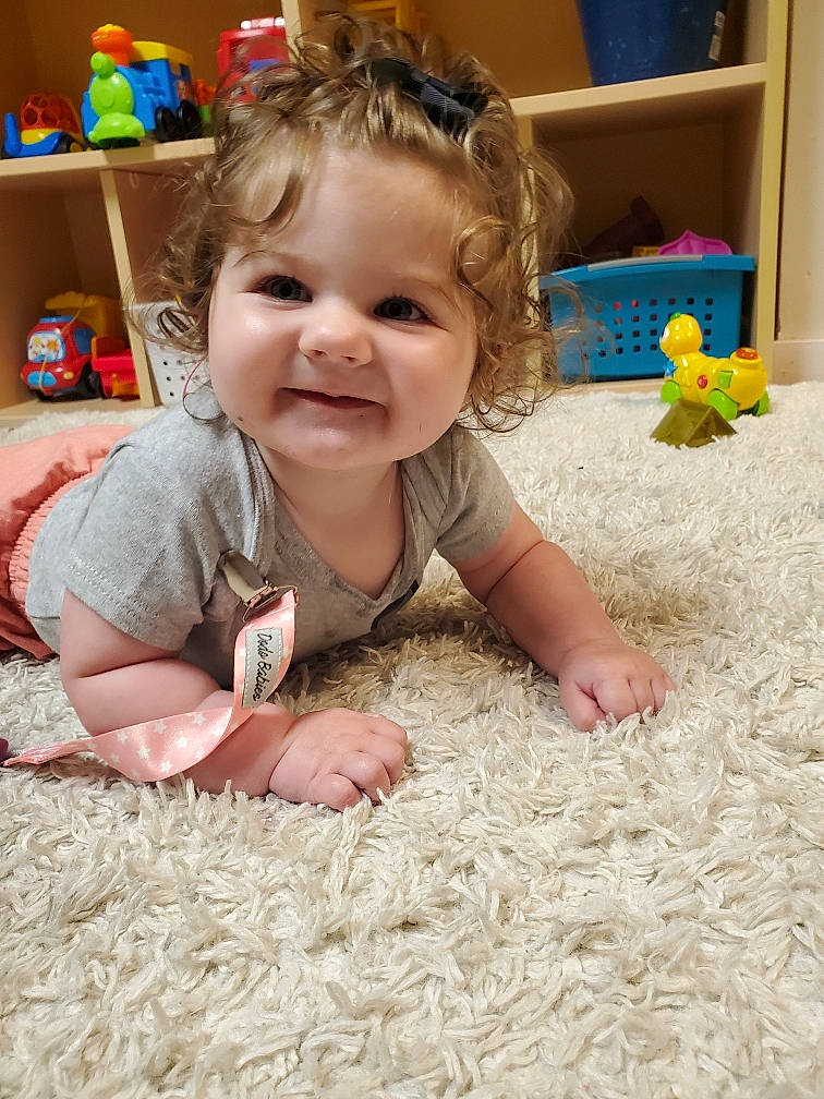 Dorothy is registered to the contest to win money with this photo: baby, baby_toddler_clothing, blue, cheek, crawling, face, facial_expression, floor, flooring, hair, head, iris, joy, nose, person, photograph, shelf, skin, smile, toddler