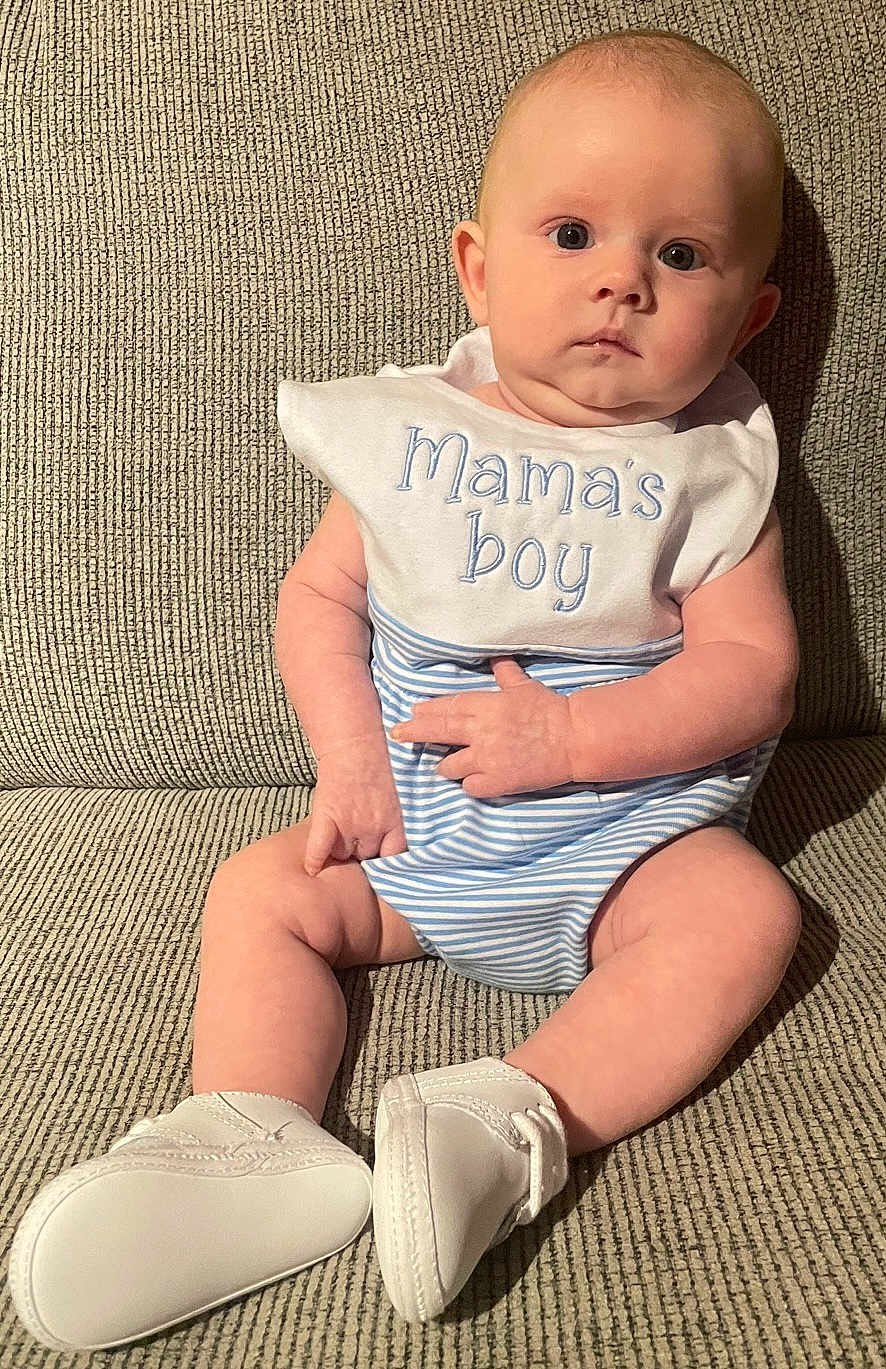 Kohen Raine joined the competition — help win amazing prizes! baby, infant, child, bib, mamas_boy, white_booties, striped_clothing, sitting, couch, beige, curious, face, hands, legs, indoor, portrait, cute, soft_light, expression, young