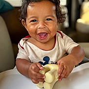 Maverick joined the competition — help win amazing prizes! baby_clothes, blurred_background, child, curly_hair, cute, face, hands, happy, indoor, joy, mouth_open, person, playful, short_sleeves, skin, smiling, squishy_toy, table, toddler, toy