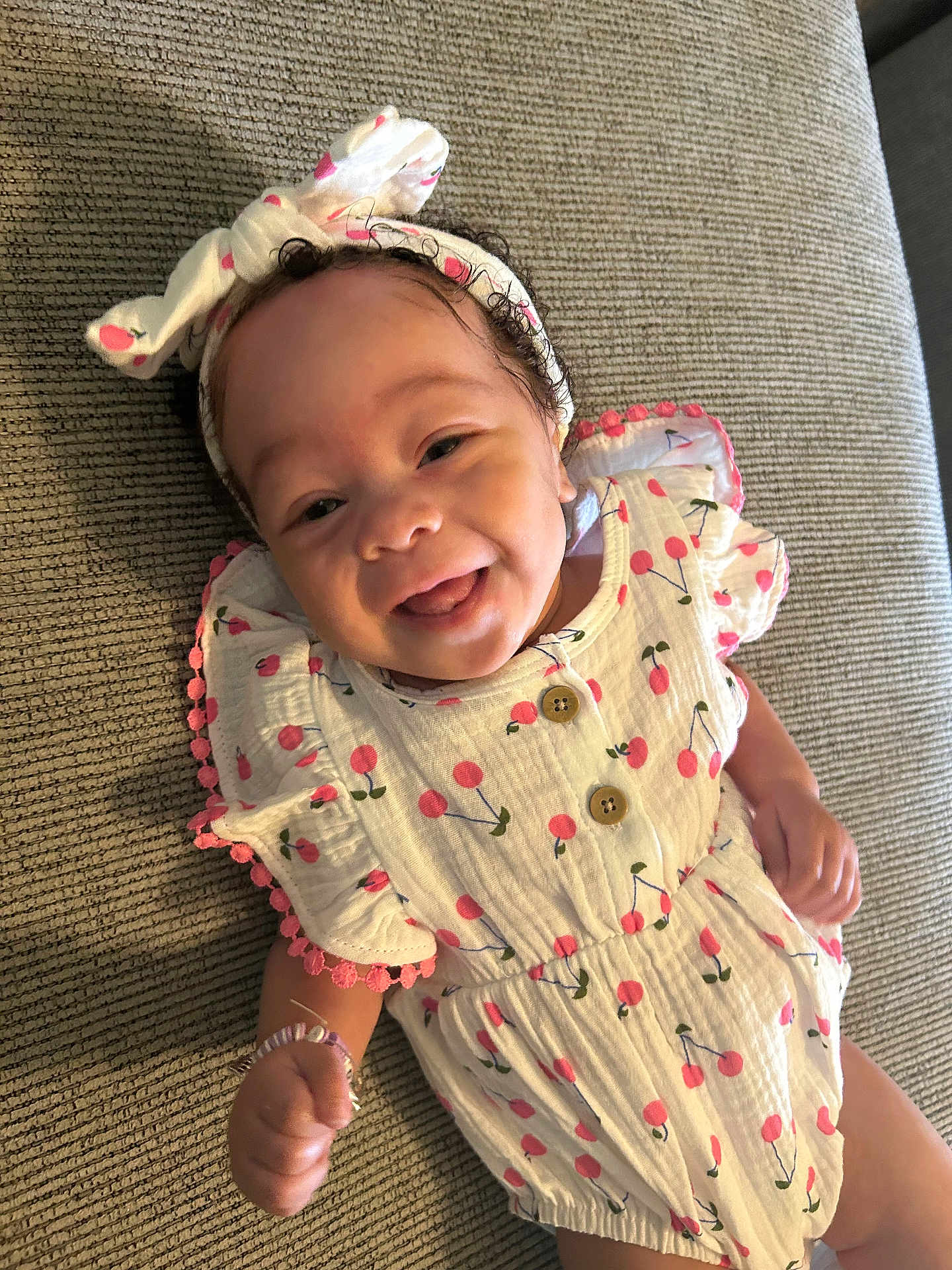 Phoenix joined the competition — help win amazing prizes! baby, child, smiling, headband, bow, cherry_pattern, clothing, cute, happy, infant, lying_down, fabric, texture, hand, bracelet, portrait, playful, indoors, person, skin