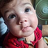 baby, close_up, face, child, curious, red_clothing, indoor, cute, big_eyes, soft_skin, infant, portrait, looking_up, expression, young_child, human, adorable, blurry_background, fan, casual