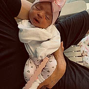 Oakley is registered to the contest to win money with this photo: newborn, baby, infant, sleeping, pink_bow, headband, swaddled, blanket, white_clothing, adult, holding, arms, tattoo, indoor, home, chairs, wood_floor, portrait, close_up, family