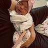 newborn, baby, infant, sleeping, pink_bow, headband, swaddled, blanket, white_clothing, adult, holding, arms, tattoo, indoor, home, chairs, wood_floor, portrait, close_up, family