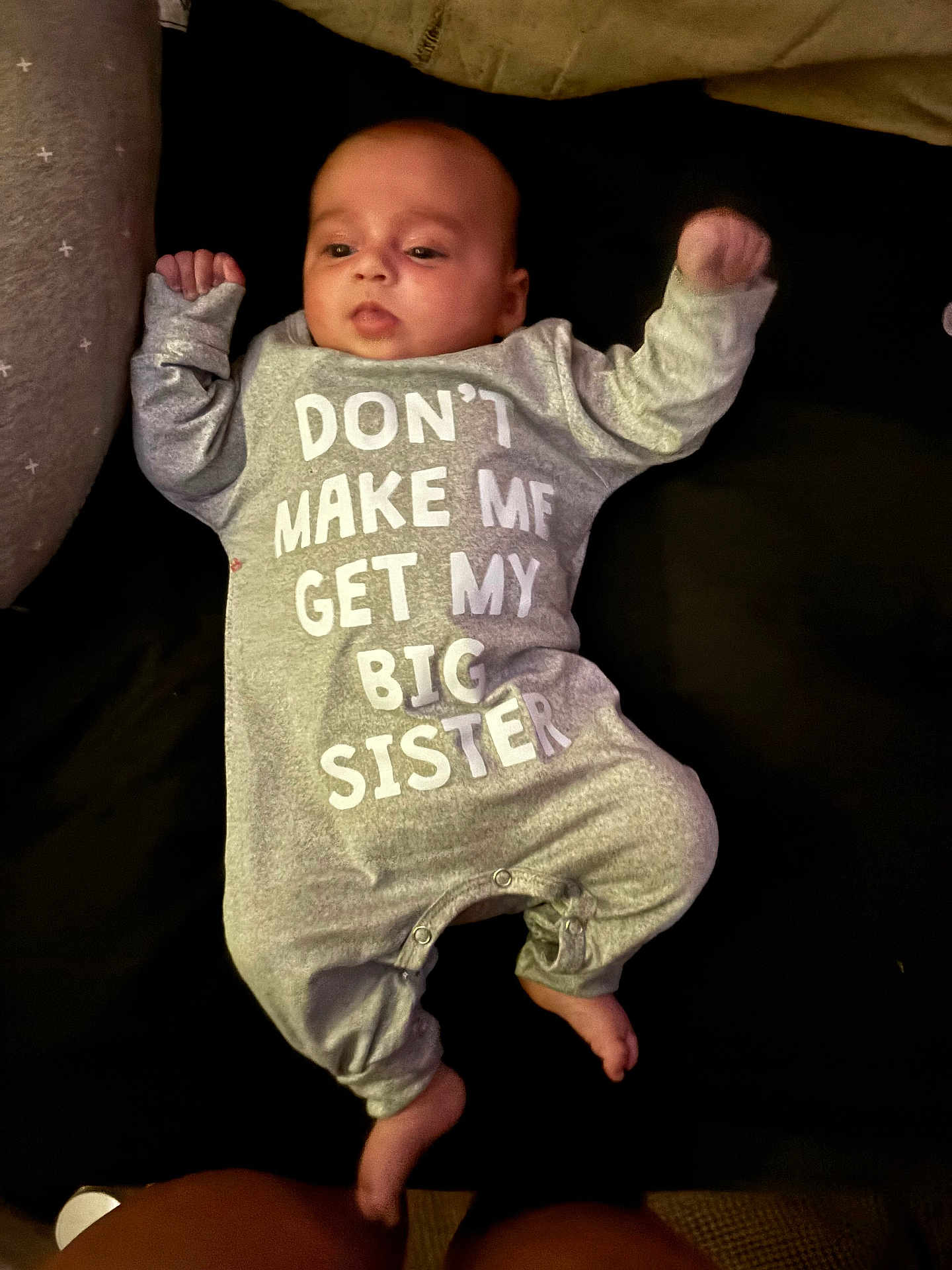 Lyndsey is registered to the contest to win money with this photo: baby, infant, onesie, clothing, lying_down, text_on_clothing, grey, white_text, hands_up, feet, face, child, cute, relaxed, indoors, soft_fabric, bed, sleepwear, person, portrait