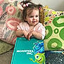book, casual, child, colorful, couch, hair_accessories, happy, home, indoor, monsters_inc, pigtails, pillow, pink_shirt, playful, reading, seated, smile, storybook, toddler, young_child