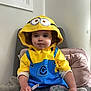 Brooklyn is registered to the contest to win money with this photo: blanket, casual_clothing, chair, child, colorful, costume, cozy, cushion, cute, face, hoodie, indoor, minion, pants, person, portrait, sitting, toddler, yellow, young_child