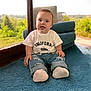 baby, child, indoor, carpet, blue_carpet, tshirt, white_tshirt, ripped_jeans, socks, sitting, smiling, face, window, natural_light, greenery, background, home_interior, wood_floor, casual_clothing, cute