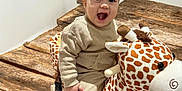 Tiago participe au concours pour gagner de l'argent avec cette photo : baby, child, plush_toy, giraffe, rocking_toy, wooden_floor, happy, smiling, indoor, sitting, clothing, beige_outfit, cute, play, fun, toy, young, person, face, wood