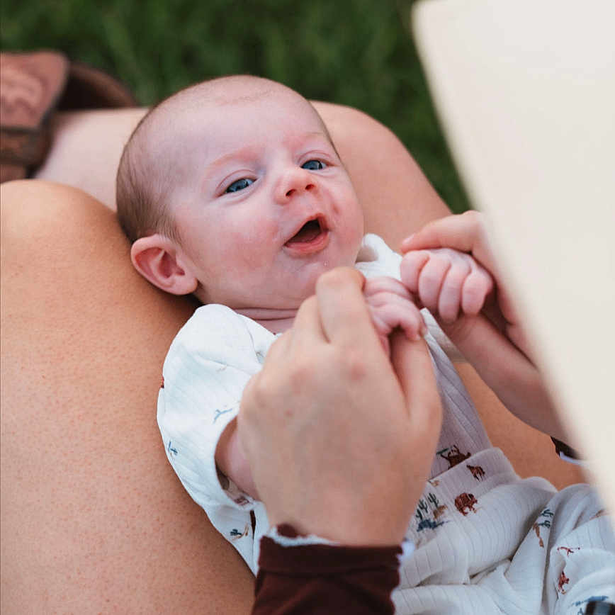 Justin joined the competition — help win amazing prizes! baby, infant, child, hands, person, lap, outdoor, grass, skin, clothing, sleeve, cow_print, holding_hands, expression, happy, cute, casual, nature, portrait, human