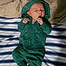 baby, newborn, infant, sleeping, green_hoodie, pants, shoes, striped_blanket, comforter, bed, clothing, person, cute, peaceful, indoors, young_child, resting, small, lying_down, cozy