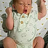 baby, newborn, infant, onesie, car_print, white_clothing, lying_down, raised_arms, curious_expression, open_mouth, bed_sheet, heart_pattern, small_hearts, cute, child, person, indoors, sleepwear, soft_lighting, human