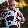 Justin joined the competition — help win amazing prizes! baby, woman, cowboy_hat, cow_print_jacket, outdoor, nature, portrait, holding, child, love, affection, warm_light, sunlight, greenery, blurred_background, person, face, head, casual_clothing, daytime