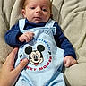baby, infant, mickey_mouse, overalls, blue_clothing, hand, blanket, soft_texture, cute, lying_down, person, newborn, small_hands, white_socks, portrait, indoor, face, head, clothing, comfort