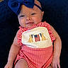 baby, child, smile, headband, blue_bow, red_stripes, onesie, embroidery, dogs, flag, cushion, indoor, portrait, cute, infant, happy, skin, hand, face, clothing