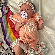 Raelynn is registered to the contest to win money with this photo: baby, pacifier, headband, bow, skirt, blanket, floral, infant, cute, clothing, lying_down, pastel_colors, fabric, soft, person, newborn, bed, toddler, smile, indoor