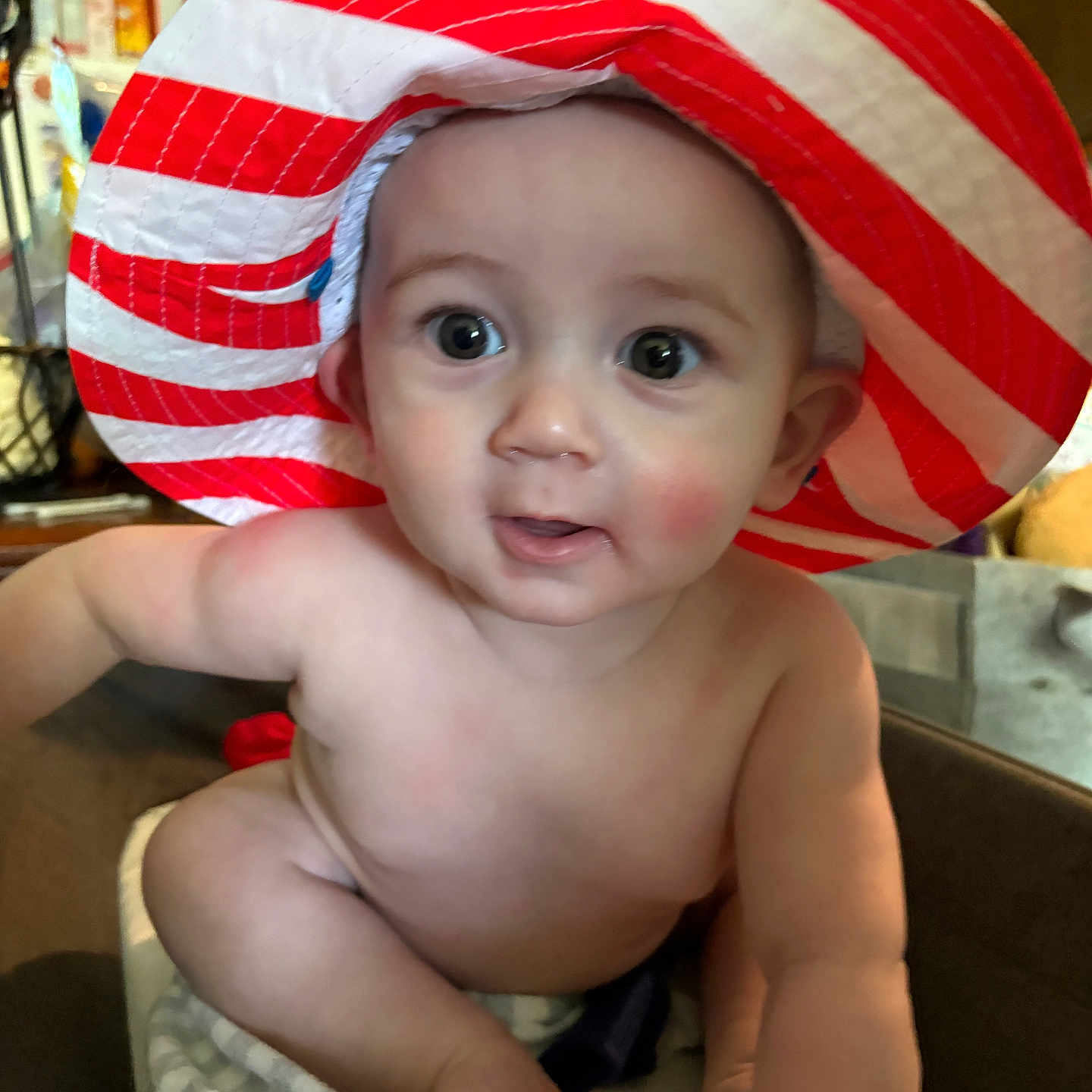 Bentley is registered to the contest to win money with this photo: arm, baby, blanket, candid, child, curious, cute, expression, eyes, face, furniture, hand, hat, indoors, infant, portrait, red_and_white, sitting, skin, striped_hat
