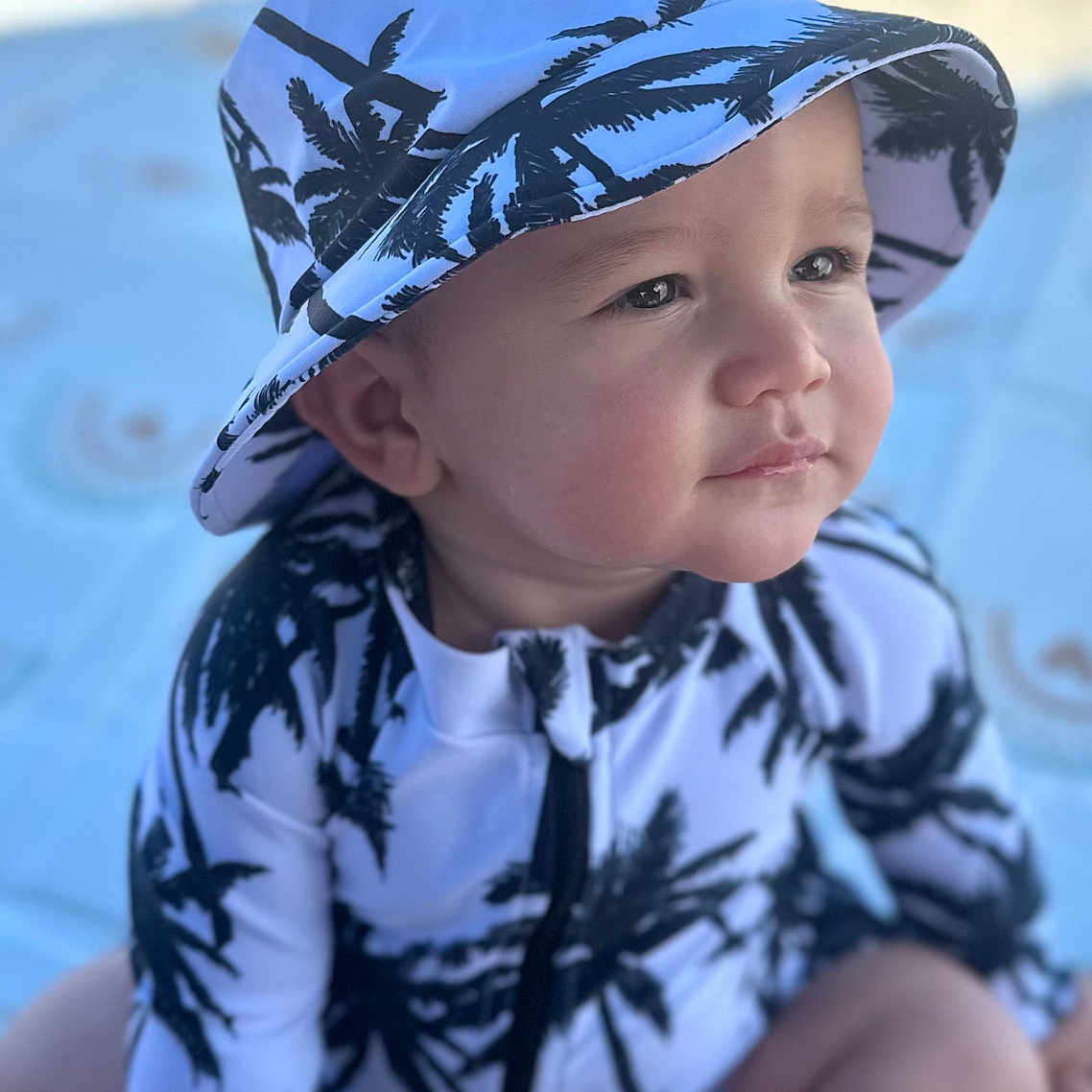 Gian Marcos is registered to the contest to win money with this photo: baby, beach, blanket, bucket_hat, child, clothing, cute, expression, face, hat, nature, outdoor, palm_tree, pattern, portrait, sitting, skin, summer, sunlight, toddler