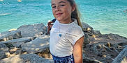 Mia a rejoint le concours — aidez-le/la à gagner de superbes lots ! child, girl, outdoor, sea, rocks, sailboats, summer, smile, white_top, blue_shorts, sunglasses, necklace, sandals, sunlight, water, sky, vacation, nature, portrait, happy