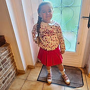 Mia a rejoint le concours — aidez-le/la à gagner de superbes lots ! child, girl, braid, smile, indoor, door, glass, floor, tile_floor, red_skirt, floral_top, socks, shoes, mat, hand_on_hip, long_hair, pose, window, wall, cozy