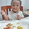 Kyrin joined the competition — help win amazing prizes! toddler, child, baby, smiling, portrait, high_chair, sitting, indoor, kitchen, meal, food, fries, chicken, cheese_sauce, table, white_shirt, curly_hair, face, hands, happy