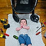 Lorena is registered to the contest to win money with this photo: baby, infant, blanket, stroller, wheel, power_drill, screwdriver, socket_wrench, ratchet, tool_set, hardwood_floor, onesie, shorts, lying_down, smiling, face, hands, indoor, playtime, workshop_tools