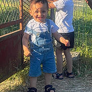 Iyaas a rejoint le concours — aidez-le/la à gagner de superbes lots ! child, boy, smiling, outdoor, sunlight, shadow, denim_overalls, tshirt, sandals, grass, metal_gate, fence, nature, play, summer, happy, two_children, portrait, daylight, casual_clothing