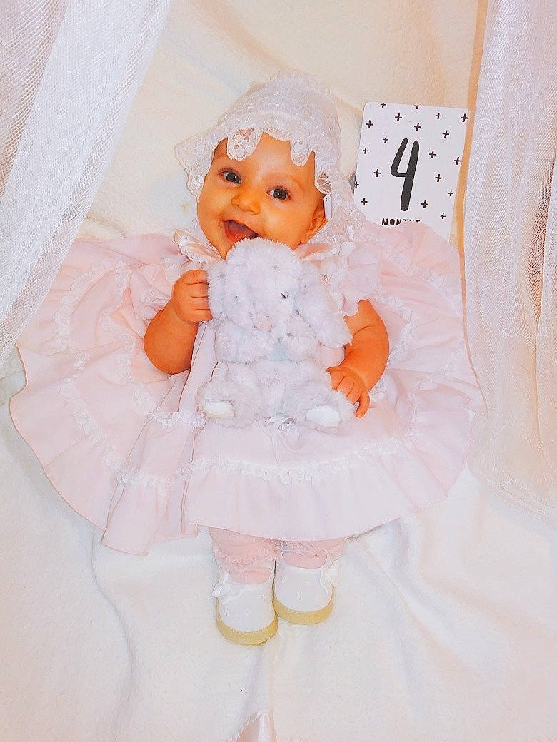 Eloise is registered to the contest to win money with this photo: bed, child, doll, girl, gown, hair_accessory, infant, person, product, textile, toddler, toy, white