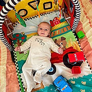 Gabriel a rejoint le concours — aidez-le/la à gagner de superbes lots ! baby, infant, play_mat, toy, soft_toy, colorful, hanging_toys, bed, blanket, smile, cute, indoor, child, person, clothing, animal_print, fabric, comfort, relaxing, early_childhood