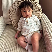 Sadie Elizabeth is registered to the contest to win money with this photo: baby, child, infant, portrait, sitting, armchair, cushion, pillow, indoor, home, cozy, clothing, dress, romper, socks, ruffles, brown_hair, blue_eyes, neutral_expression, photography