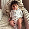 baby, child, infant, portrait, sitting, armchair, cushion, pillow, indoor, home, cozy, clothing, dress, romper, socks, ruffles, brown_hair, blue_eyes, neutral_expression, photography