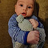 Jayce joined the competition — help win amazing prizes! baby, child, infant, striped_clothing, blue_clothing, stuffed_animal, plush_toy, couch, brown_furniture, face, hands, portrait, indoor, cute, soft_toy, expression, young_child, seated, person, cozy
