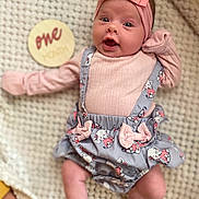 Maria joined the competition — help win amazing prizes! baby, infant, one_month, headband, pink_bow, cute_outfit, gray_dress, pink_shirt, blanket, lying_down, milestone, wooden_sign, wide_eyes, surprised_expression, soft_lighting, indoors, closeup, adorable, child, portrait