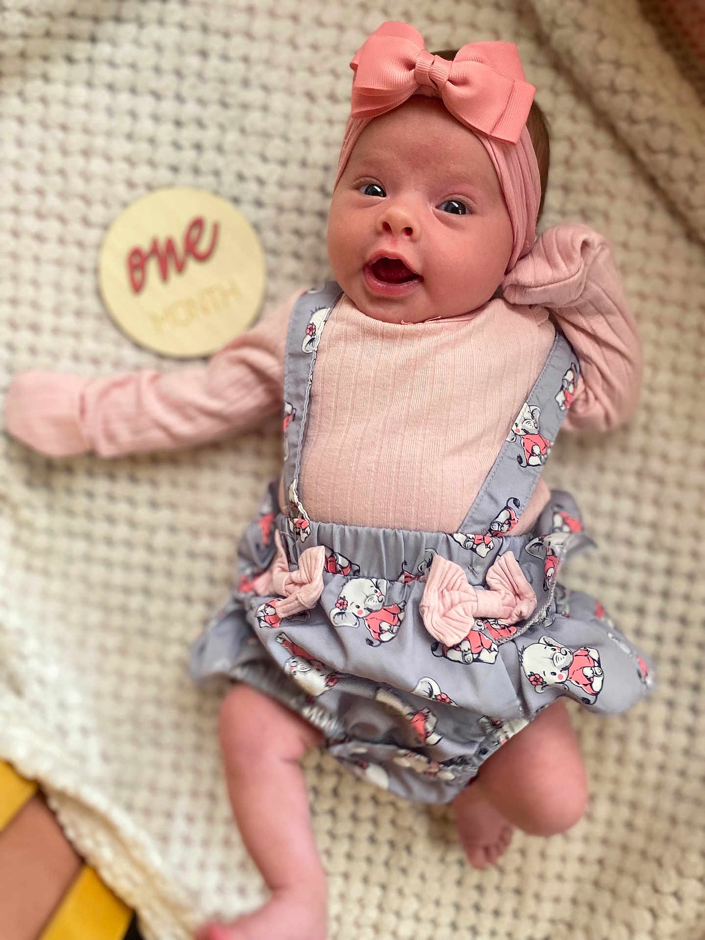 Maria joined the competition — help win amazing prizes! baby, infant, one_month, headband, pink_bow, cute_outfit, gray_dress, pink_shirt, blanket, lying_down, milestone, wooden_sign, wide_eyes, surprised_expression, soft_lighting, indoors, closeup, adorable, child, portrait