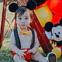 toddler, child, mickey_mouse, balloons, outdoor, grass, toy, costume, headwear, bow_tie, red_shorts, suspenders, black_ears, plush_toy, pouting, sitting, sunlight, playful, cute, portrait