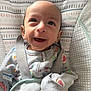 baby, smiling, infant, onesie, baby_seat, bib, patterned_clothing, happy, face, cute, child, indoors, baby_accessory, closeup, infant_clothing, seat_strap, fabric_pattern, soft_toy_pattern, light, portrait