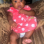 Eliayne Cacho joined the competition — help win amazing prizes! baby, child, infant, dress, pink, polka_dot, couch, sofa, brown, patterned, furniture, indoor, foot, hand, curious, wide_eyes, person, seated, home, cute