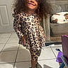 child, toddler, smiling, portrait, indoor, standing, dress, leopard_print, leggings, shoes, curly_hair, fashion, dog, chair, furniture, tile_floor, home, playroom, pet, happy