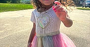 Sapphirerose is registered to the contest to win money with this photo: child, girl, curly_hair, smiling, portrait, outdoor, sunny, sky, clouds, dress, tulle_skirt, rainbow_colors, pink, hand_gesture, suburban, driveway, house, car, grass, summer