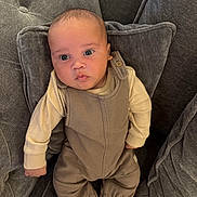 Roman is registered to the contest to win money with this photo: baby, infant, child, face, eyes, clothing, overalls, long_sleeve, stripes, chair, cushion, gray, plush, comfortable, indoors, portrait, sitting, cute, expression, soft