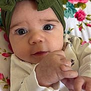 Aurora joined the competition — help win amazing prizes! baby, infant, face, headband, green_bow, hand, eyes, white_clothing, floral_blanket, close_up, cute, child, portrait, indoors, soft_lighting, skin, expression, newborn, person, lying_down