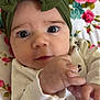 baby, infant, face, headband, green_bow, hand, eyes, white_clothing, floral_blanket, close_up, cute, child, portrait, indoors, soft_lighting, skin, expression, newborn, person, lying_down