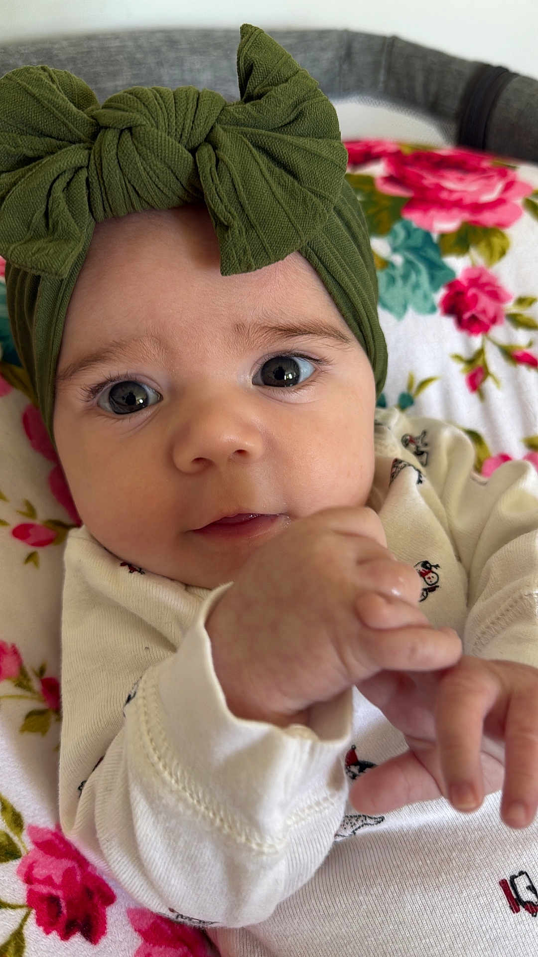 Aurora joined the competition — help win amazing prizes! baby, infant, face, headband, green_bow, hand, eyes, white_clothing, floral_blanket, close_up, cute, child, portrait, indoors, soft_lighting, skin, expression, newborn, person, lying_down